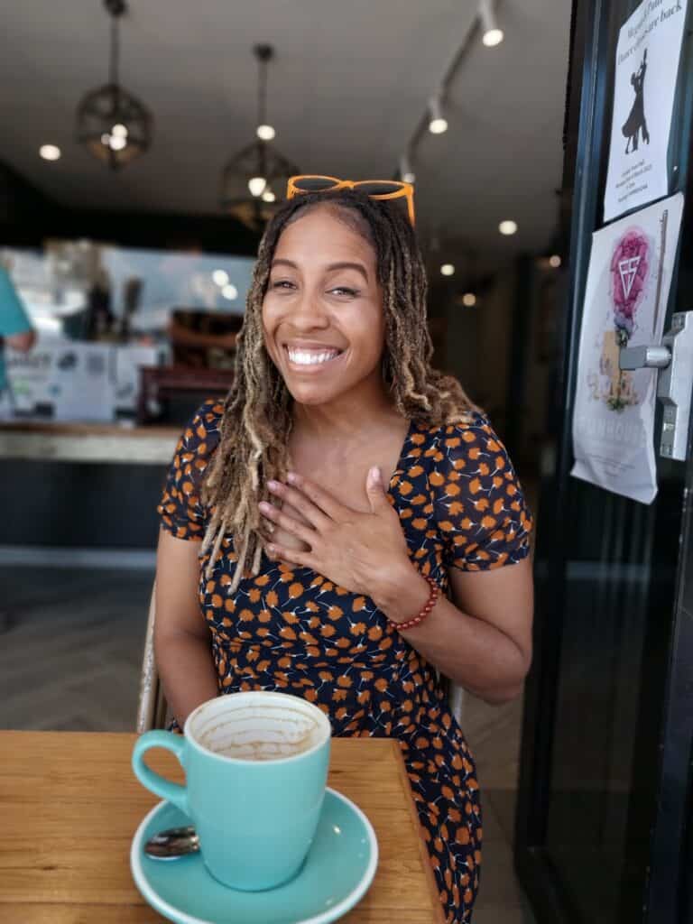 Image of a woman sitting in a coffee shop with a coffee mug in front of her.