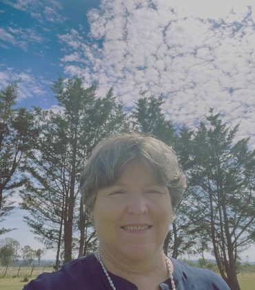 Woman smiling outside with trees in the background