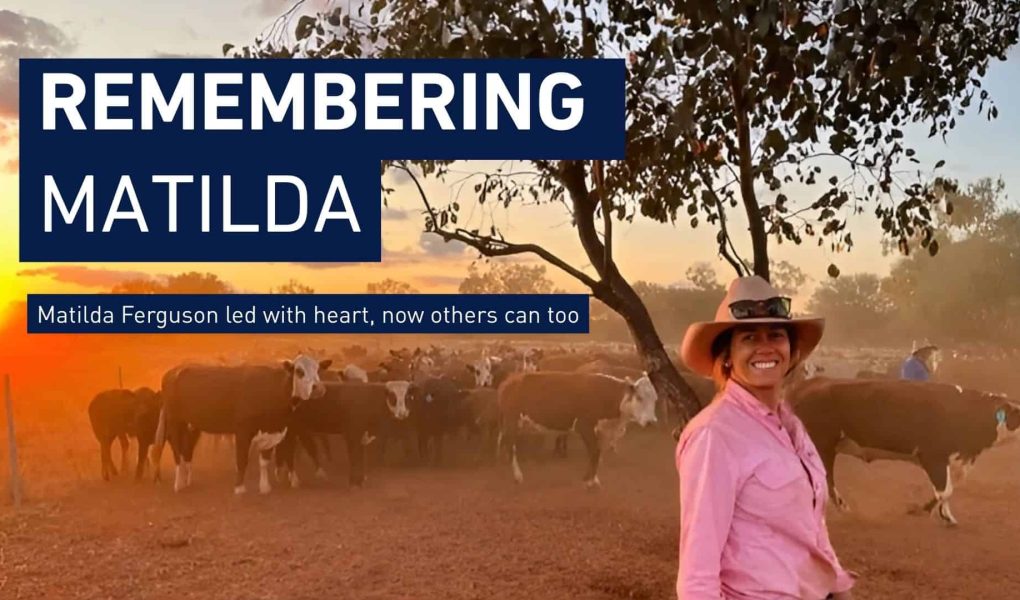 A young woman in a pink shirt and stands in a dusty cattle yard. Above her reads the text 'Remembering Matilda'